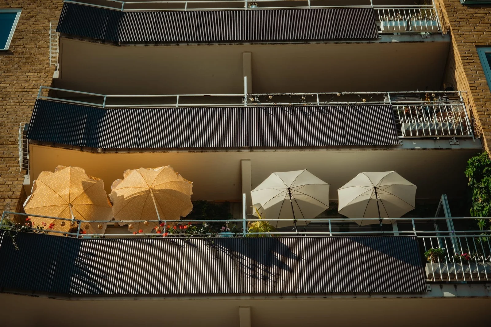 Yellow and white parasols line a sunlit balcony on a brick apartment building.