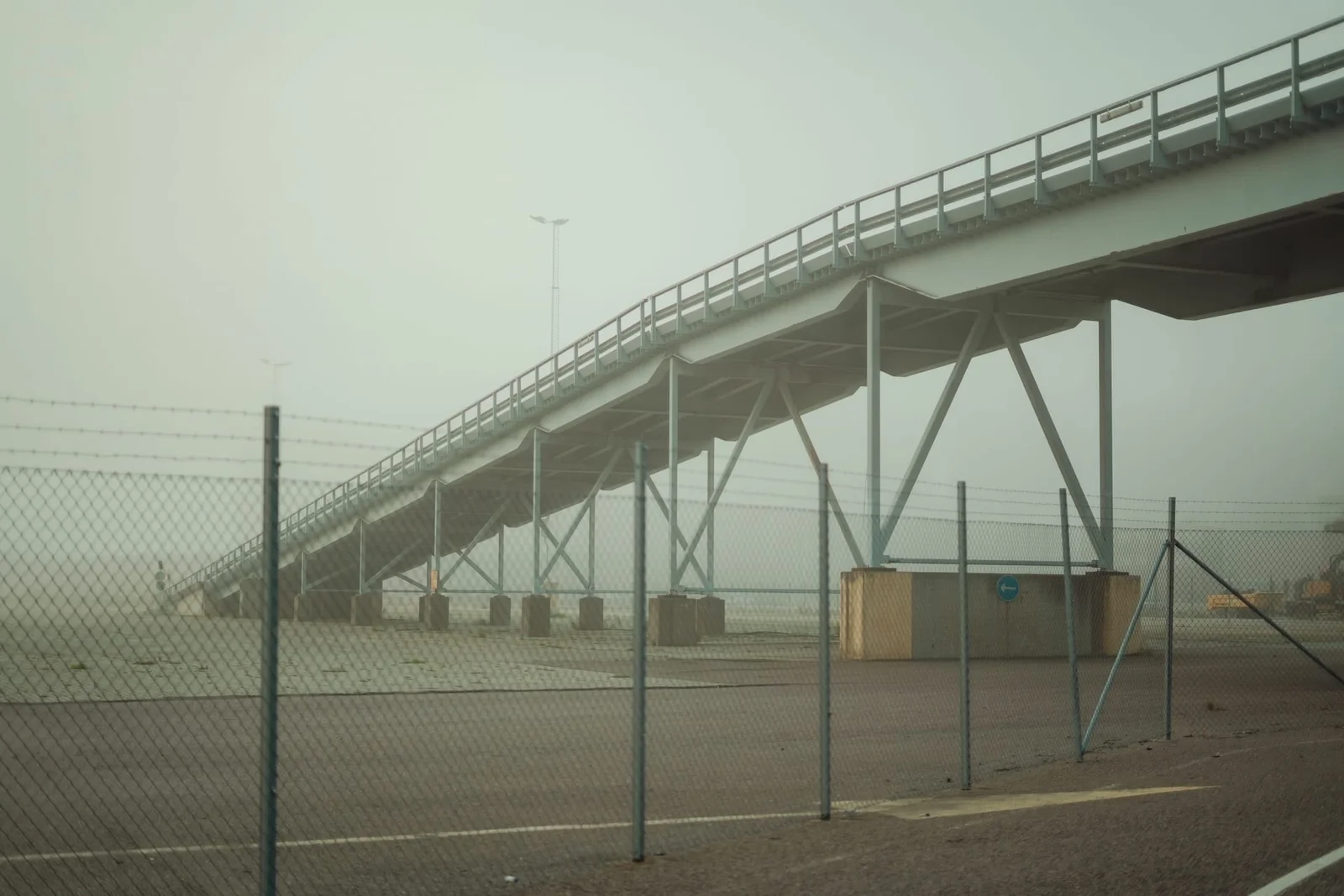 An elevated concrete walkway above a fenced area in pale, misty light.