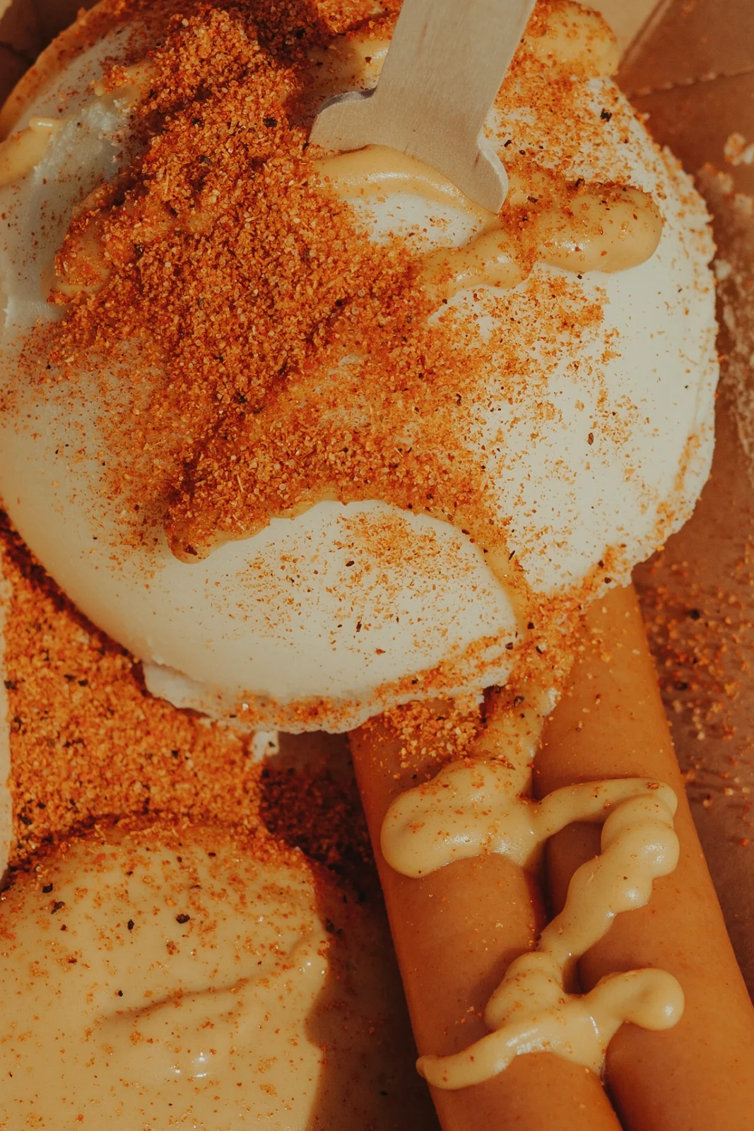 A fried egg sprinkled with red seasoning beside sausages and mustard.