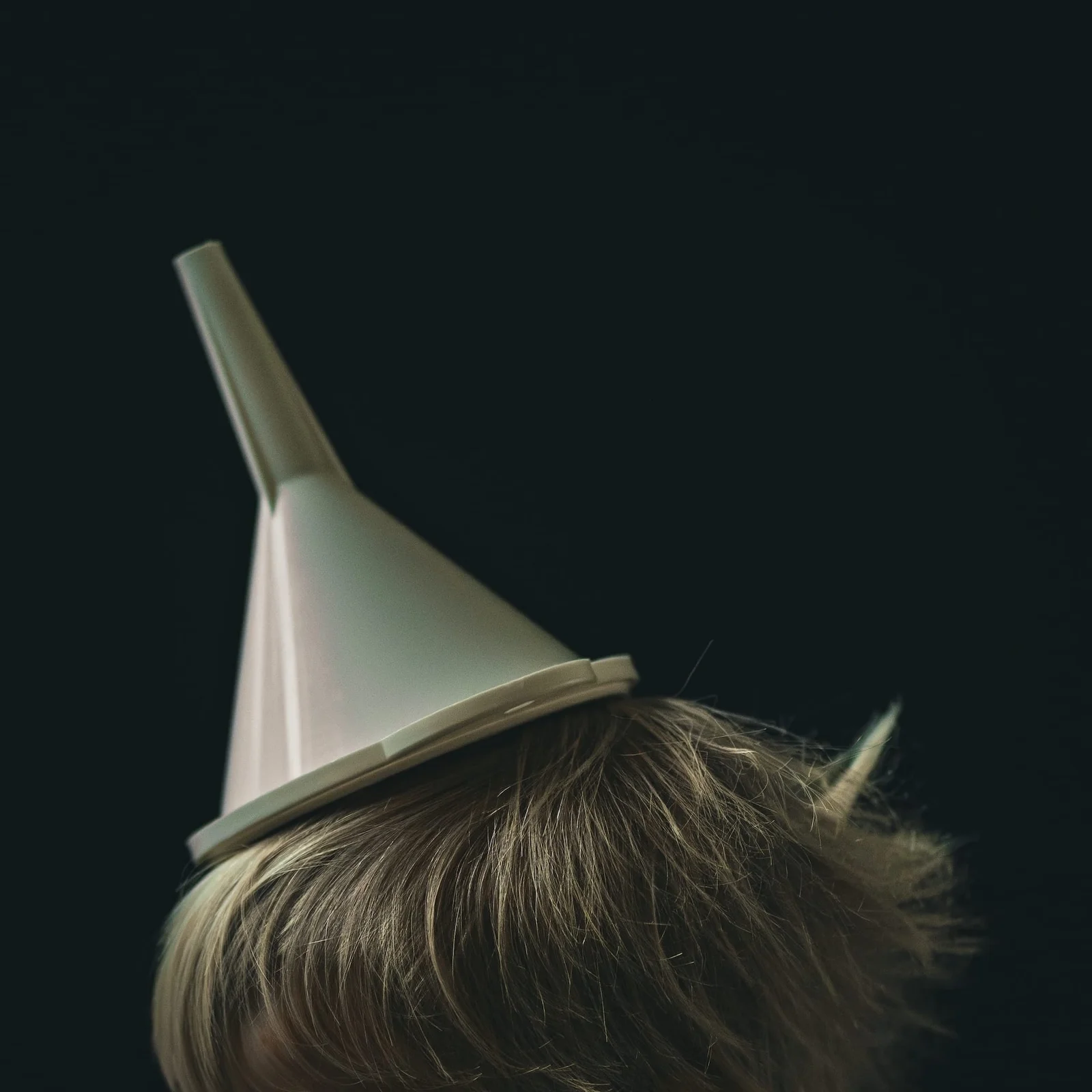 A metal funnel rests on a child’s head against a dark background.